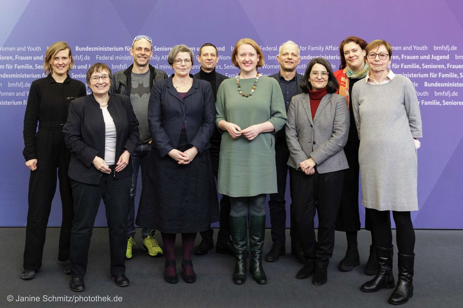 Zehn Personen stehen vor einem farbigen Hintergrund