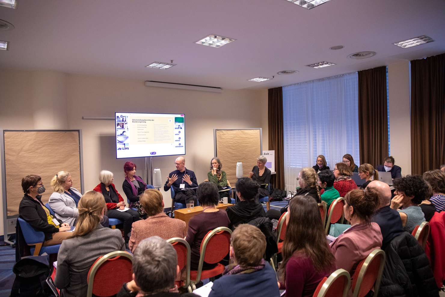 Eine Gruppe von Menschen diskutiert in einem Raum vor einem Publikum